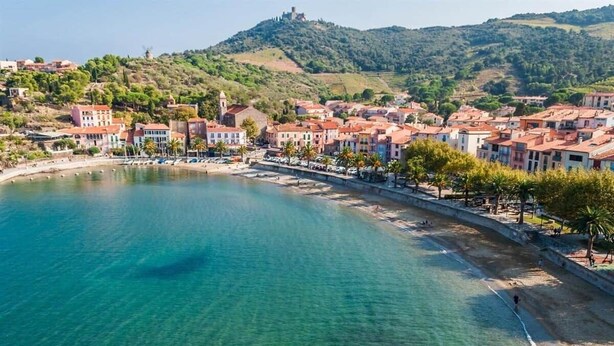 Une ville côtière dotée d’une baie aux eaux limpides, de bâtiments historiques et d’une colline surmontée d’un château.