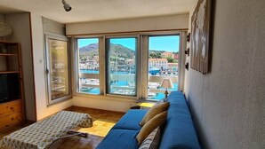 Un salon avec un canapé bleu, des meubles en bois, un téléviseur et de grandes fenêtres donnant sur une marina.
