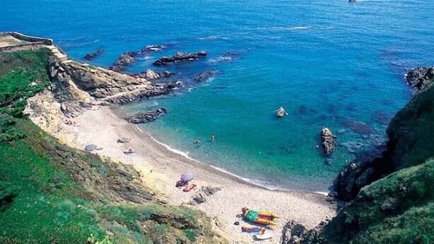 Une plage côtière bordée de formations rocheuses et aux eaux d’un bleu limpide.