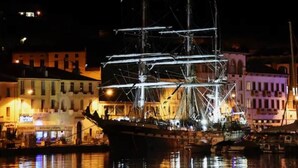 Un navire à voile historique est amarré dans un port, avec des bâtiments en arrière-plan.