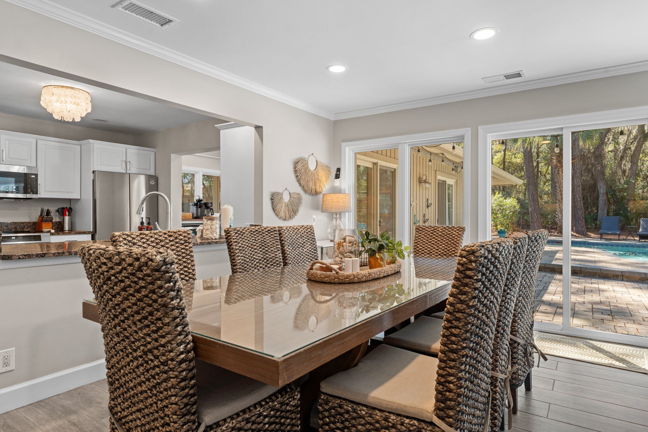 A modern kitchen with white cabinets, stainless steel appliances, and a dining area with woven chairs and a glass table.