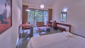 Ein Hotelzimmer mit einem großen Bett, einem Schreibtisch, einem Stuhl, einer Couch und Blick ins Freie.