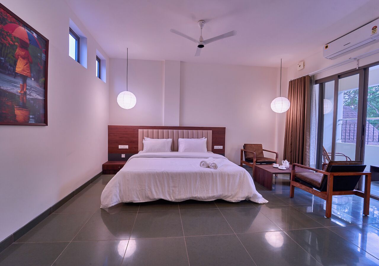 A hotel room with a large bed, bedside tables, a chair, a desk, and a large window.
