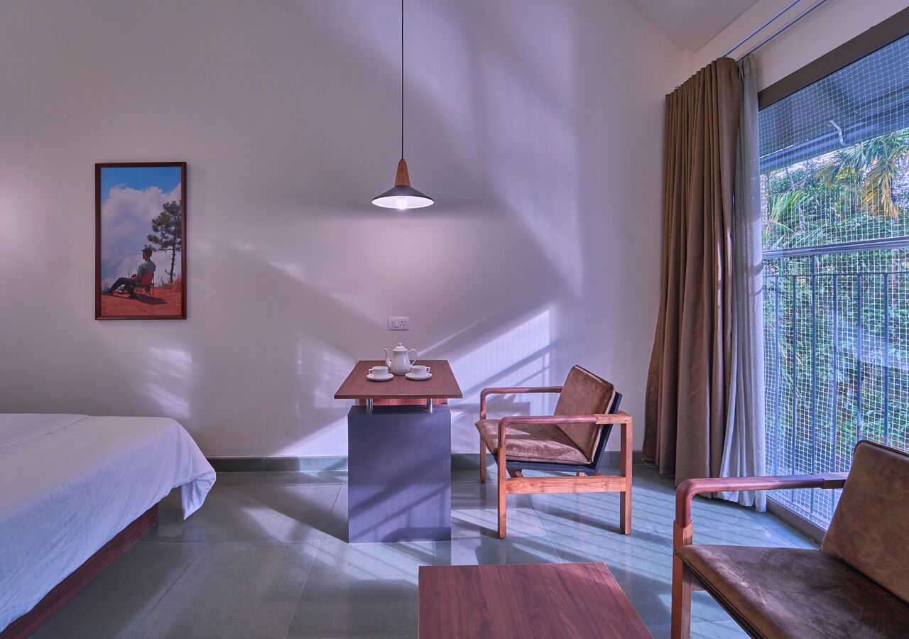 Ein Hotelzimmer mit einem Bett, einem Schreibtisch mit Stuhl, einer Pendelleuchte und einem großen Fenster mit Vorhängen.