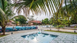 Una piscina con plataforma de baldosas, rodeada de palmeras y un mural.