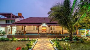 Un hotel con un camino empedrado que lleva a la entrada, rodeado de plantas tropicales y una palmera.