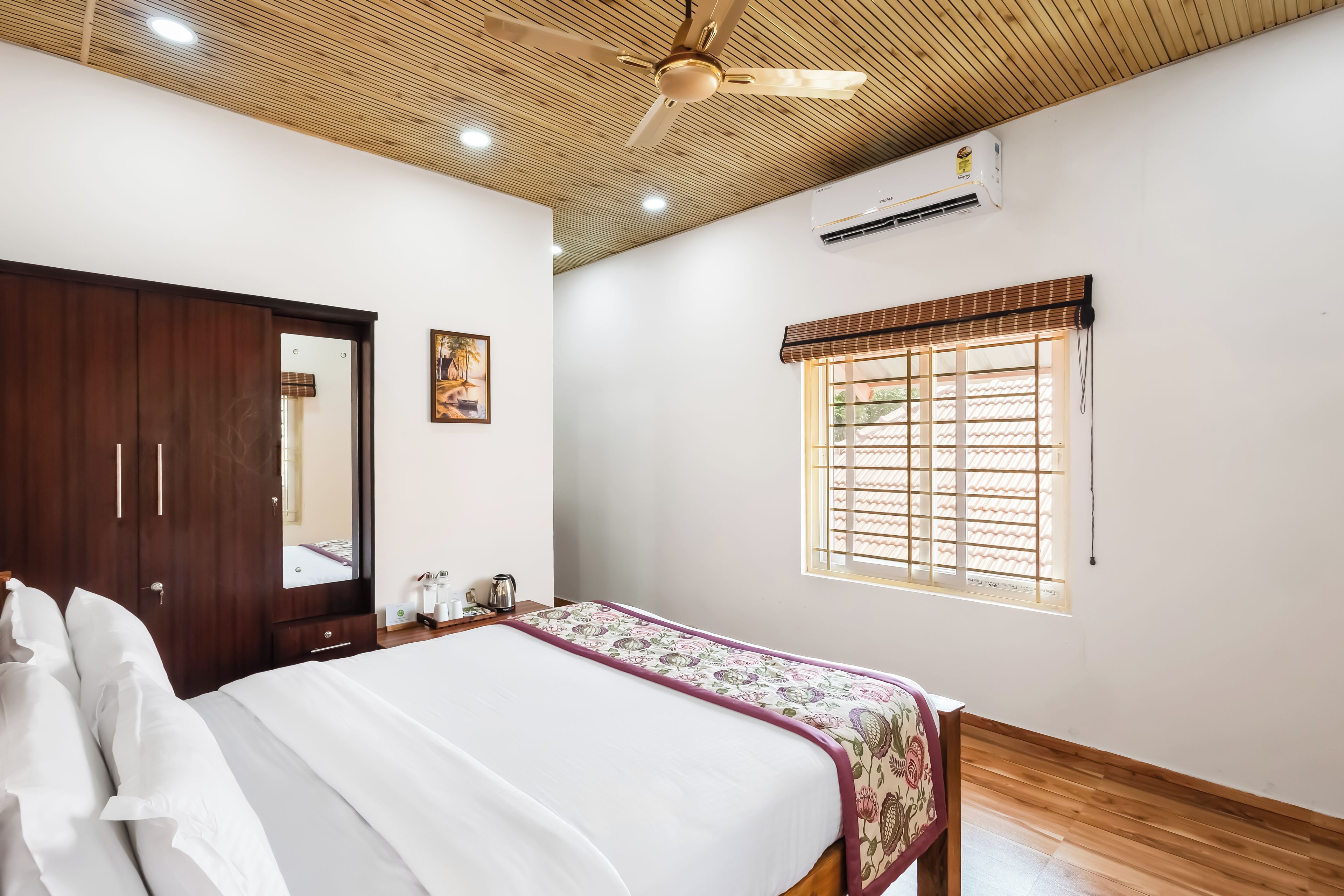 A bedroom with a bed, a wardrobe, a ceiling fan, an air conditioning unit, and a window with a view.
