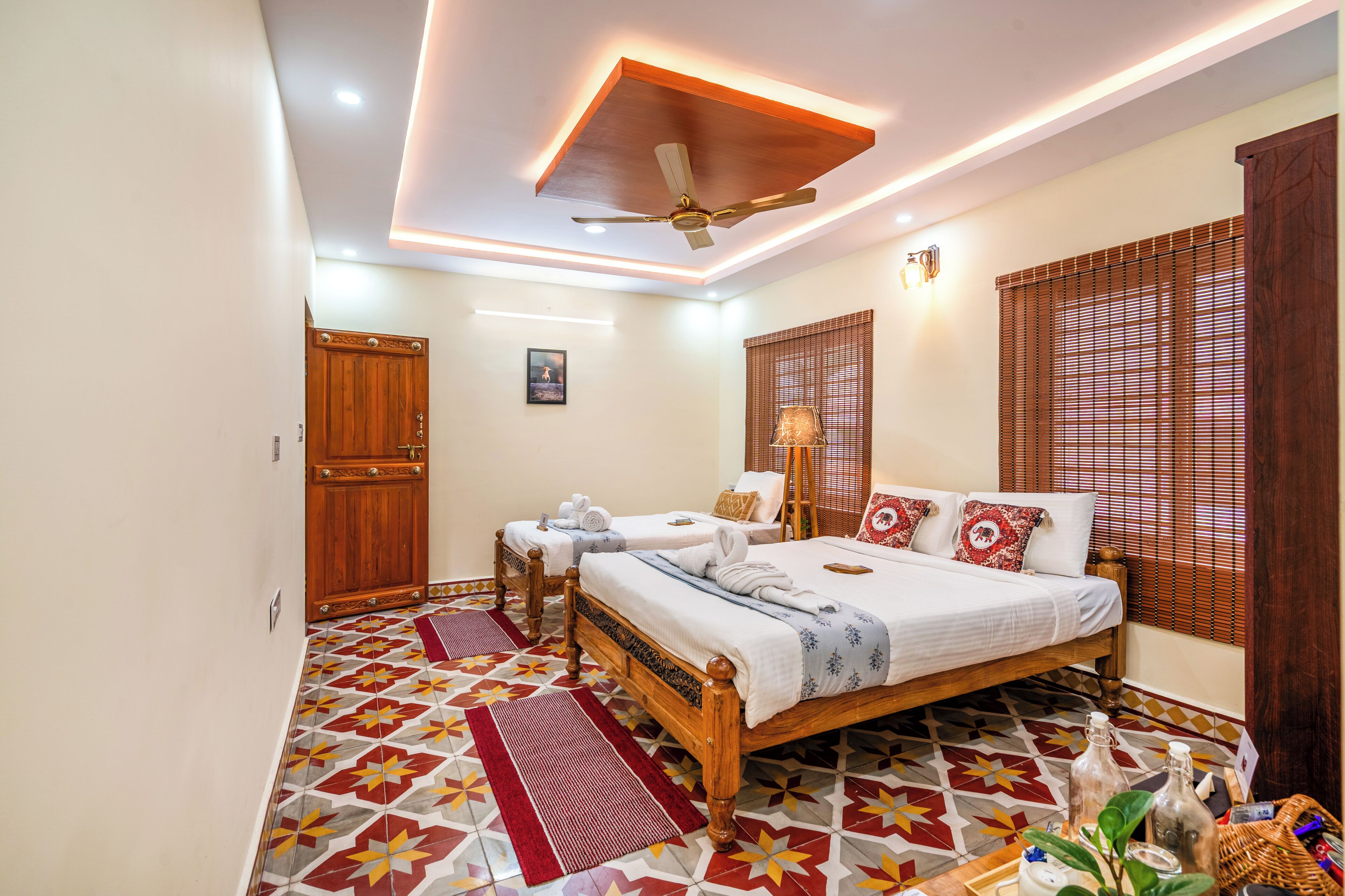 A hotel room with a large bed, two smaller beds, a ceiling fan, and a patterned floor.