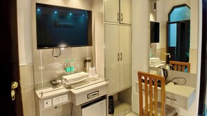 Un baño moderno con un espejo grande, un televisor sobre el lavamanos y un refrigerador compacto.