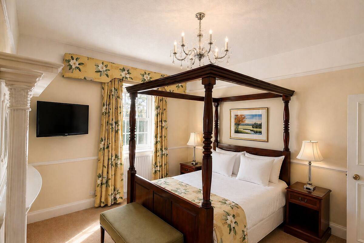 Una cama con dosel, una lámpara de araña, un televisor en la pared y un cuadro sobre la cama.