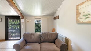 A living room with a brown leather sofa, a wooden ceiling, a window with a view, and a door. - Rural Apartment El Corral 1 (Lladurs)