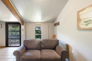 A living room with a brown leather sofa, a wooden ceiling, a window with a view, and a door. - Rural Apartment El Corral 1 (Lladurs)