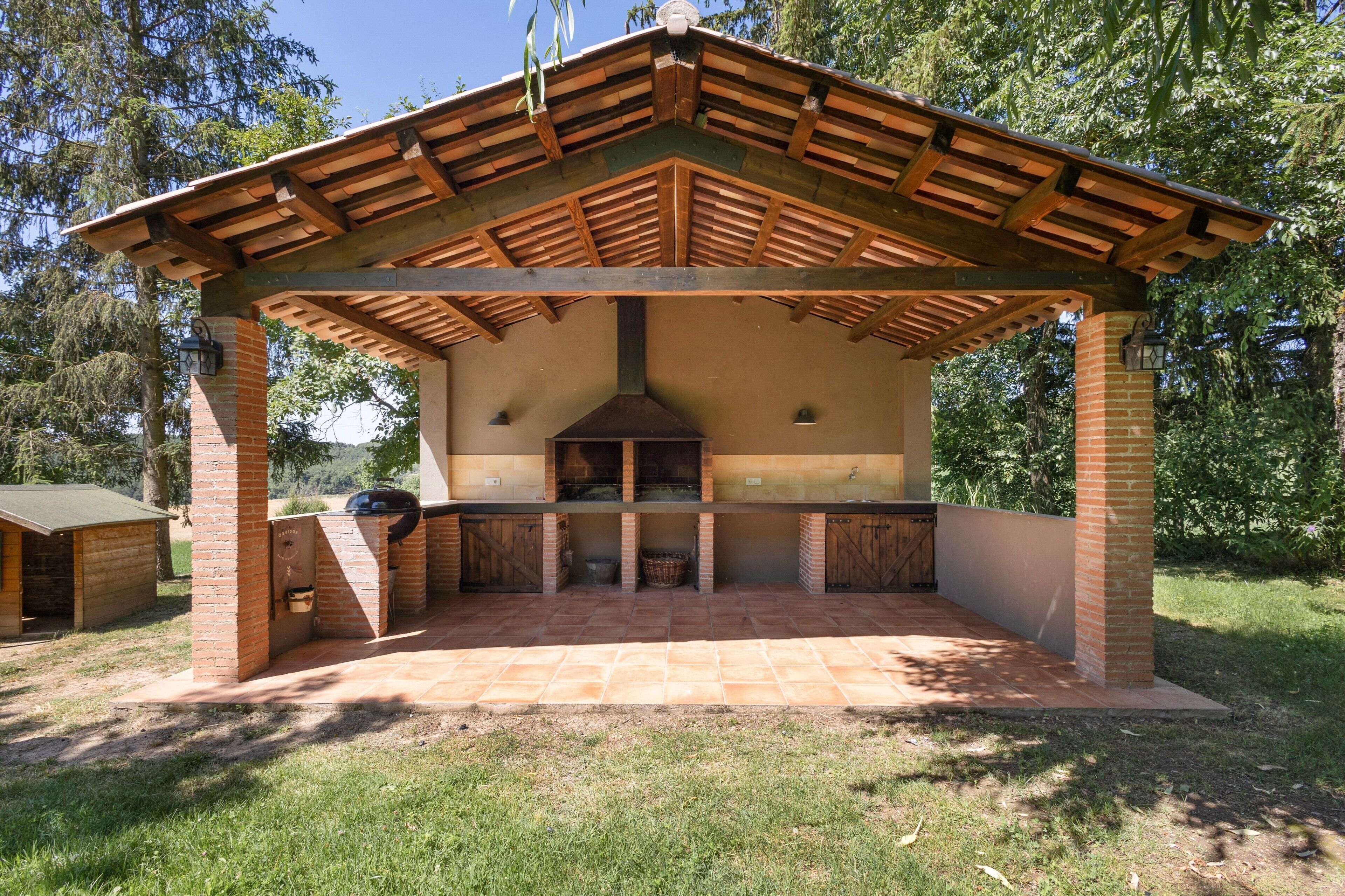 A covered outdoor barbecue area with a brick chimney, a grill, and a tiled floor.