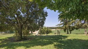 A park with a playground, including a slide and swings, surrounded by trees and grass. - Rural Apartment El Corral 1 (Lladurs)