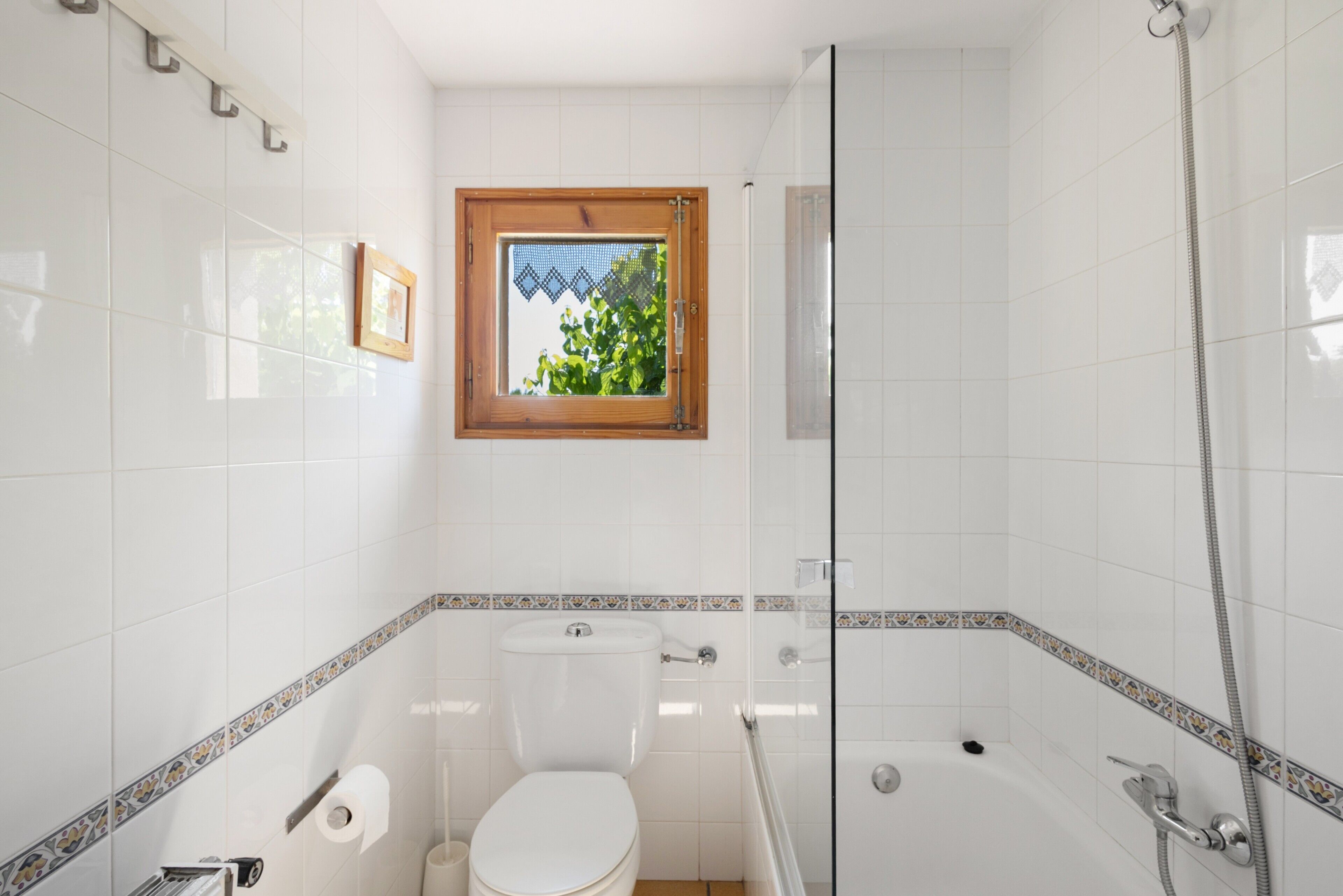 A bathroom with a toilet, a shower, a bathtub, and a window with a view of greenery.