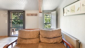 Et værelse med en træbænk, en radiator, et indrammet billede af fugle og et vindue med udsigt over grøn vegetation.