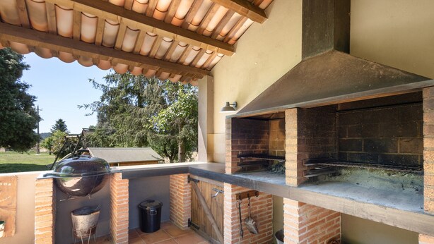Et udendørs køkken med grill, murstensovn og pergola.