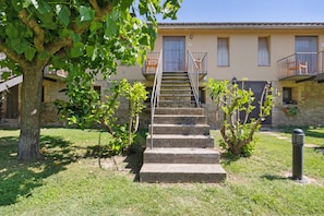 A building with a stone staircase leading to a balcony, surrounded by greenery and a tree. - Rural Apartment El Corral 2 (Lladurs)