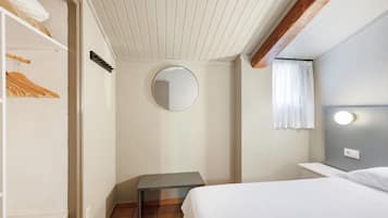 Un dormitorio con cama, mesita de noche, espejo, armario y ventana con cortinas.