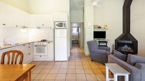 A kitchen with white cabinets, a microwave, and an oven. There is a dining table with chairs. A living area with a sofa and a TV is visible. A fireplace is present in the living area. - Rural Apartment El Corral (Lladurs)