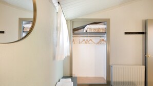 A bedroom with a bed, a bedside table, a mirror, a radiator, and a closet with hanging clothes. - Rural Apartment El Corral (Lladurs)