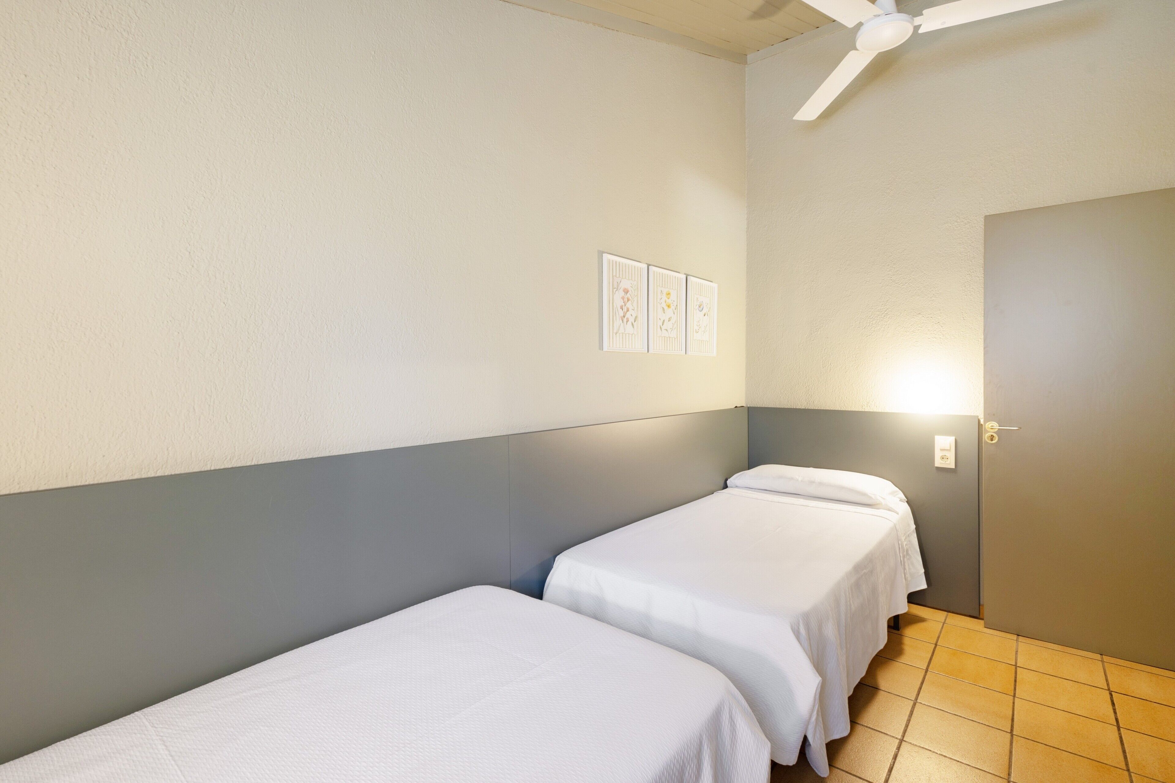 Une chambre d’hôtel avec deux lits simples, un ventilateur de plafond, un luminaire et une porte.
