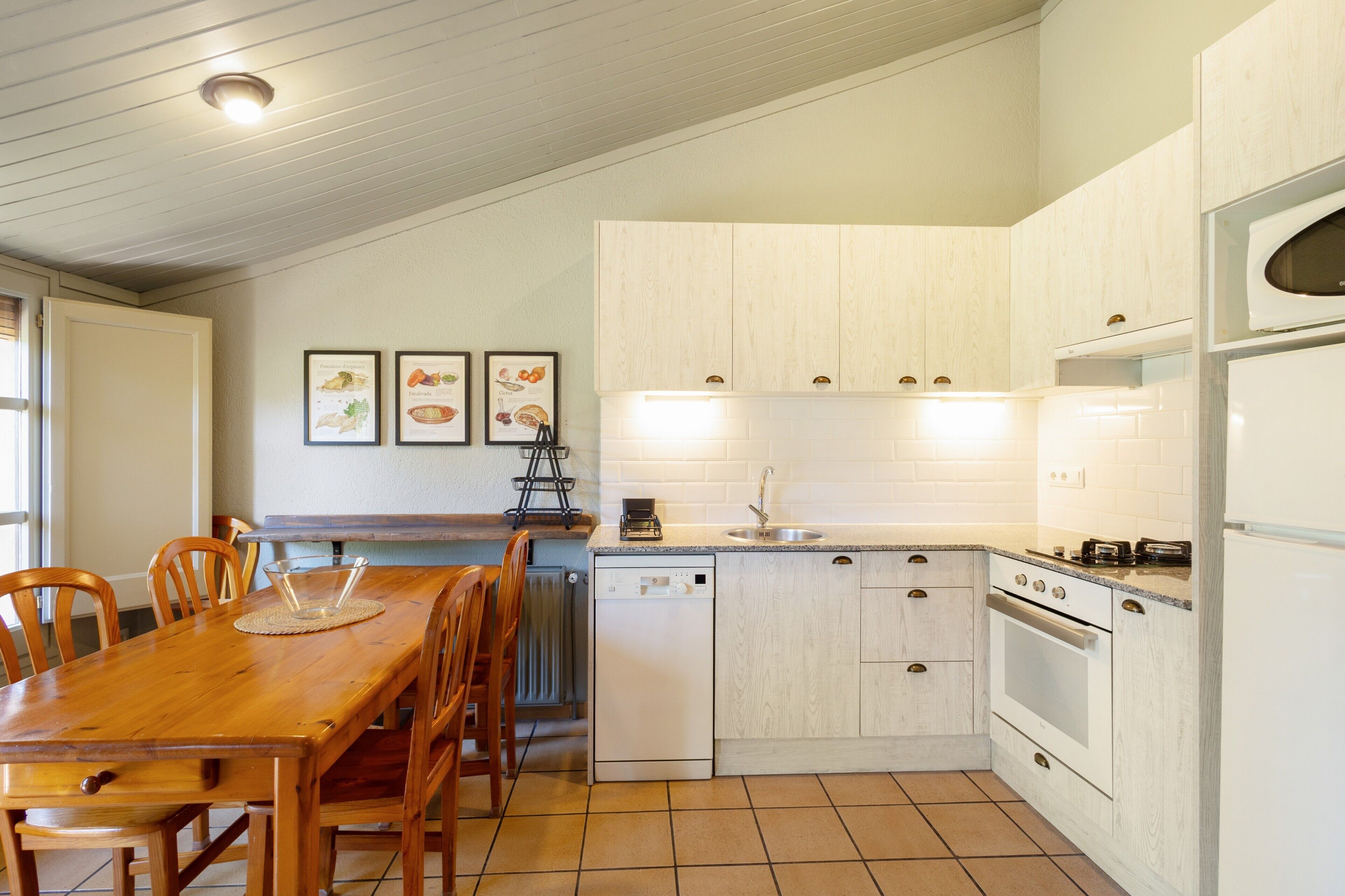 Una cocina con armarios blancos, lavavajillas, horno y una mesa de comedor con sillas.