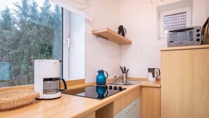 Cocina compacta con cafetera, hervidor, microondas y ventana con vistas a árboles.