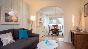 Una sala de estar con sofá, una mesa de centro, una mesa de comedor y una zona de cocina con armarios y una lámpara.