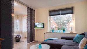 Una sala moderna con un sofá, una mesita, un televisor y un ventanal con vistas a edificios.