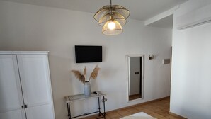 A bedroom with a bed, a wardrobe, a bedside table with a vase and pampas grass, a mirror, and a mounted TV. - Hotel Pozo Rey by youroom (Chipiona)