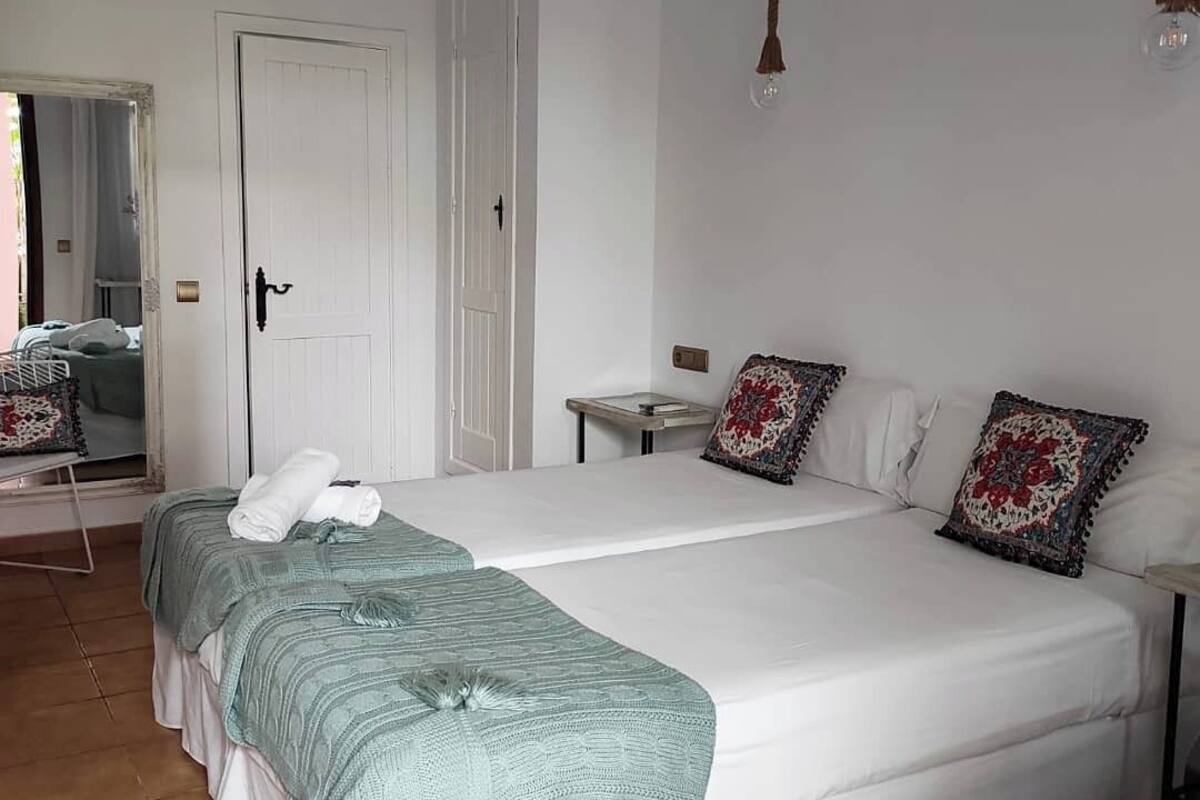 A bedroom with two beds, a bedside table, a hanging light fixture, and a door.