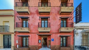 A multi-story building with balconies, a blue sign, and a visible entrance. - Hotel Pozo Rey by youroom (Chipiona)