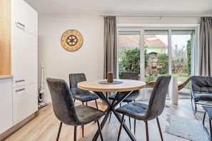 A modern kitchen with a round dining table, four chairs, a clock, and a view of a garden through a sliding glass door. - Apartment 'Carmen' with Shared Terrace, Private Garden and Wi-Fi (Wiek)