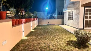 A well-maintained outdoor area with a lawn, potted plants, and a building with a brick facade. - Narpati Villa (Jodhpur)