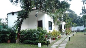 A white building with a tiled roof, surrounded by lush greenery and potted plants. - Anandam Farms And Resort (Haridwar)