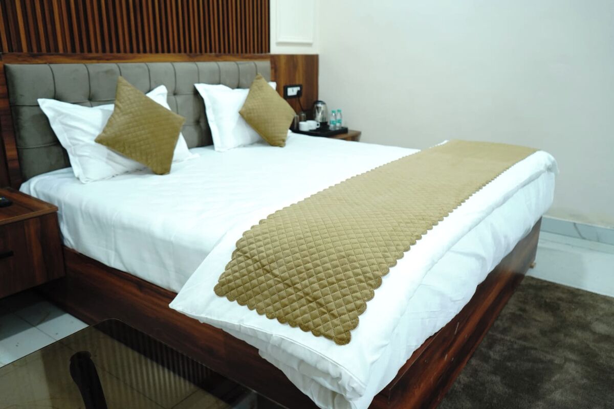 Un letto rifatto con una coperta bianco e beige, una testiera in legno e un comodino con una lampada e un piccolo tavolino.