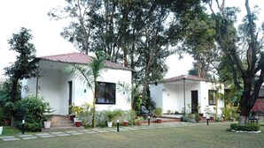 A two-story white building with a red roof, surrounded by lush greenery and trees. - Anandam Farms And Resort (Haridwar)