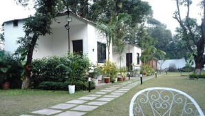 A white building with a paved pathway leading to a white chair. - Anandam Farms And Resort (Haridwar)