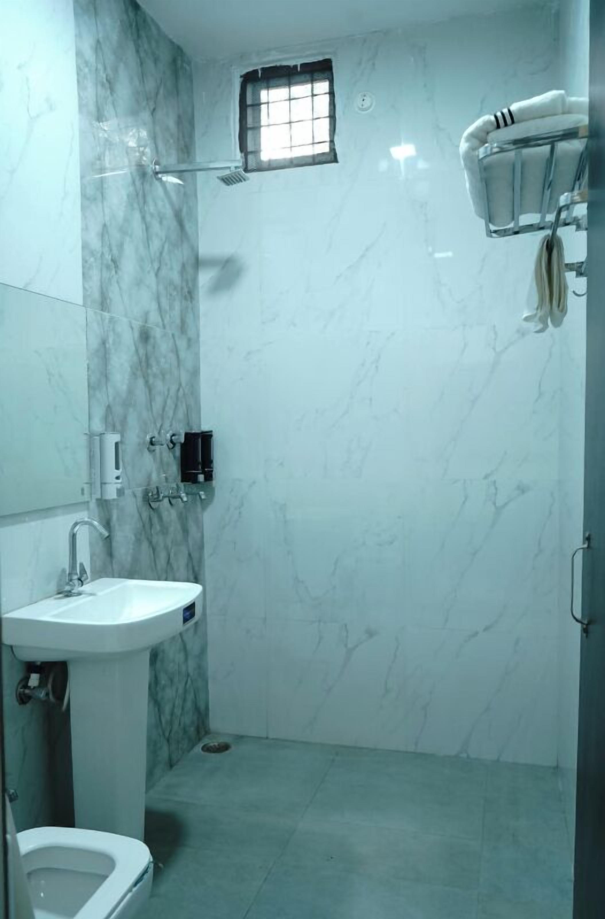 A bathroom with a marble wall, a sink, a toilet, and a shower.