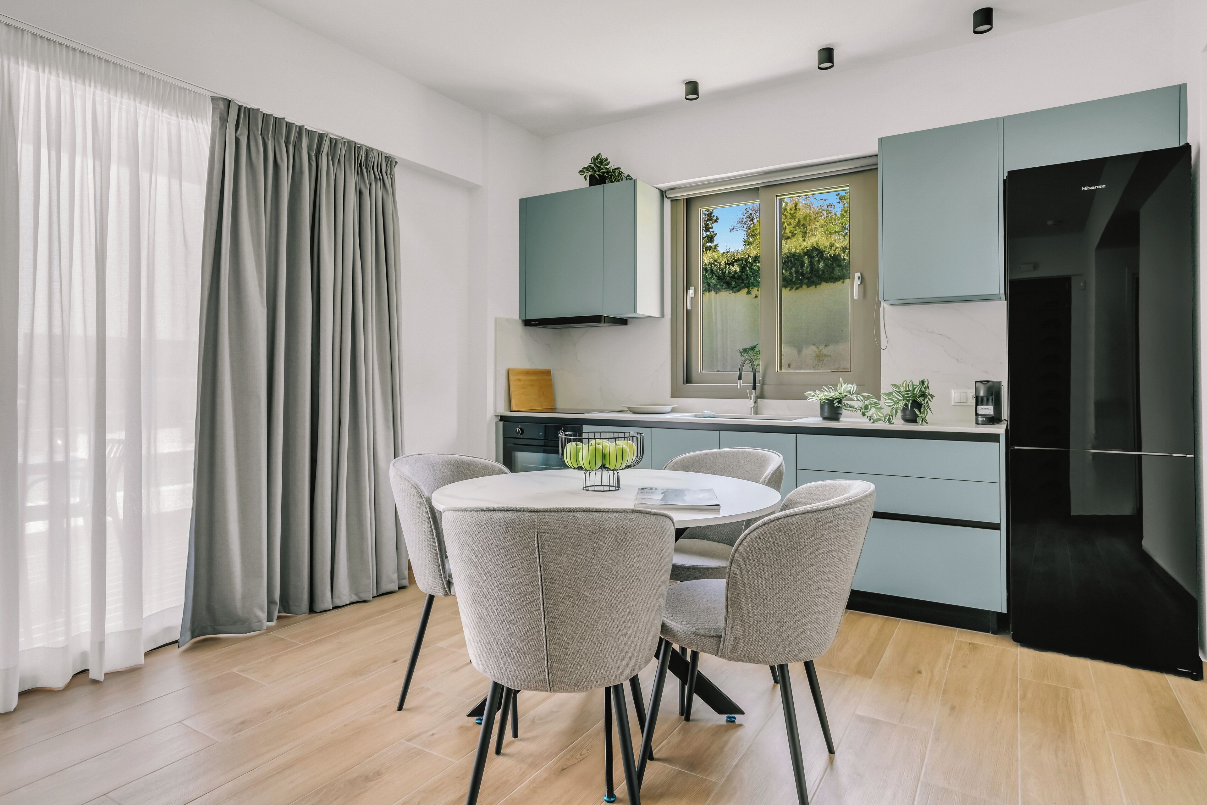 Een moderne keuken met een ronde eettafel en stoelen, een inbouwoven en een raam met uitzicht op groen.