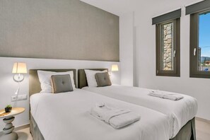 A hotel room with two beds, a stone wall, and a window with a view. - Olearia Villas (Malevizi)