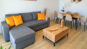 Ett modernt vardagsrum med en grå hörnsoffa, ett soffbord i trä och en matplats med ett bord och stolar i trä.