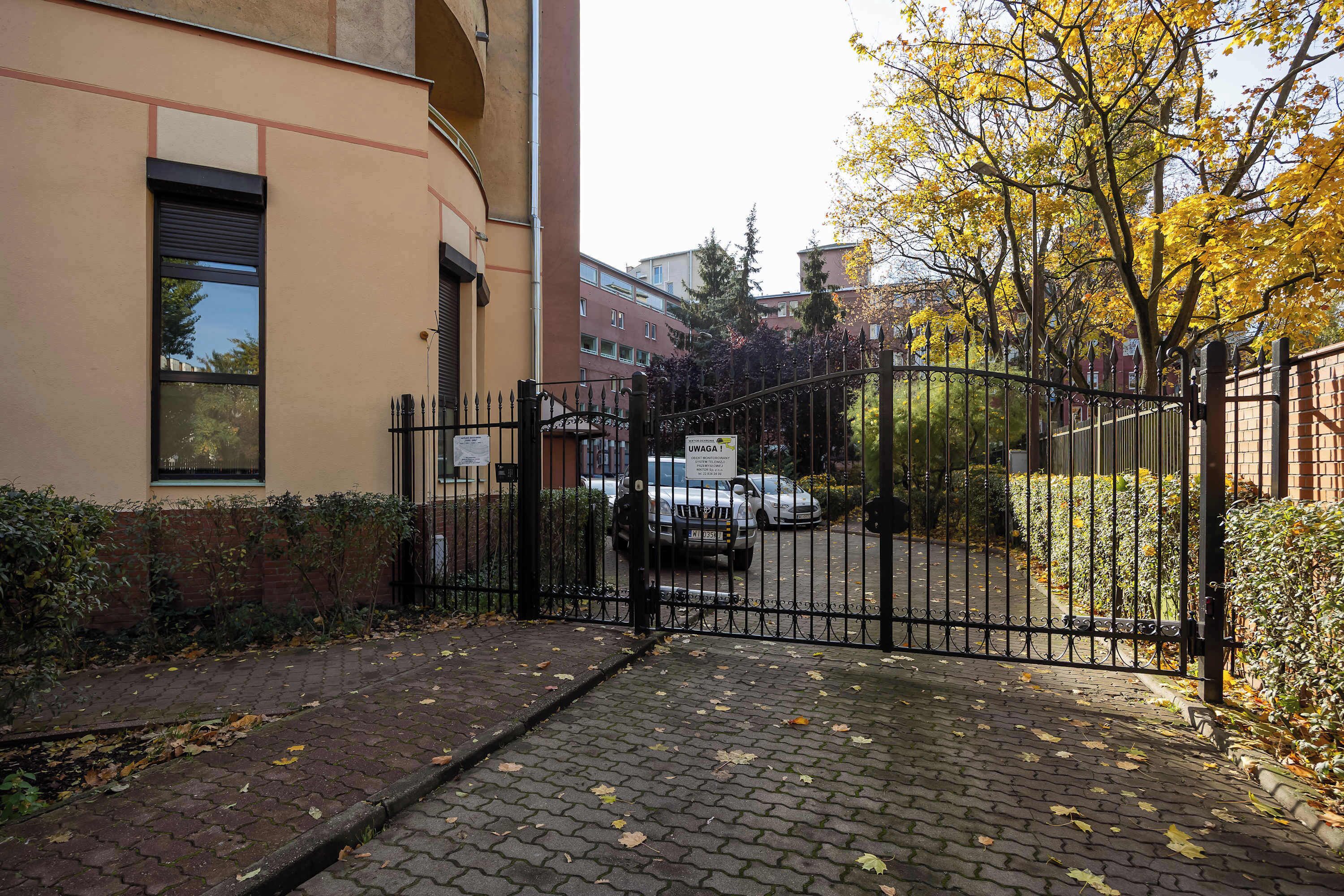 Une entrée fermée par un portail donnant accès à un immeuble, avec un chemin pavé et un véhicule stationné.