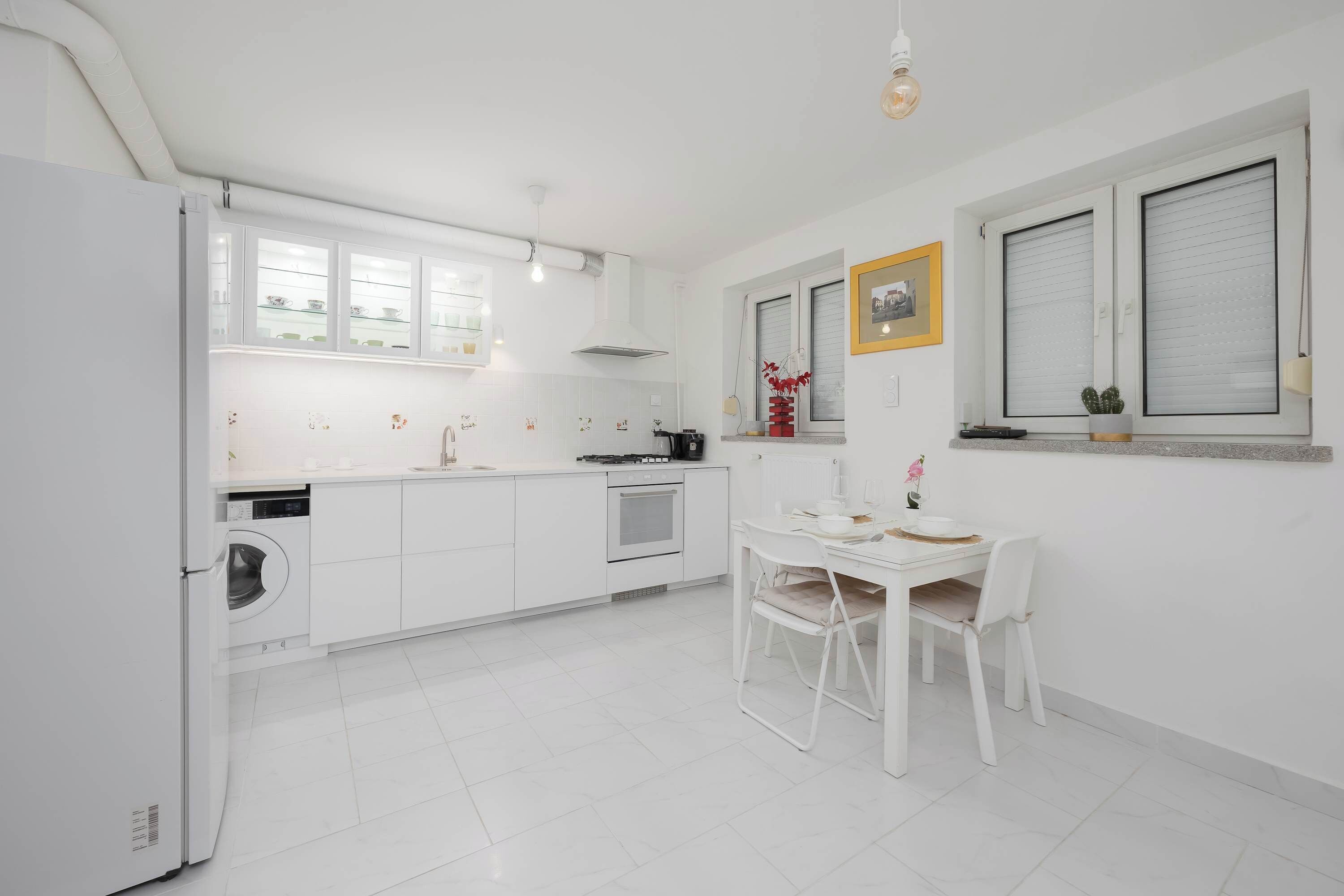A modern kitchen with white cabinetry, a built-in oven, and a dining area with a white table and chairs.