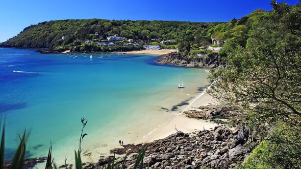 Un paisaje costero con una playa arenosa, aguas azules cristalinas y un litoral rocoso.