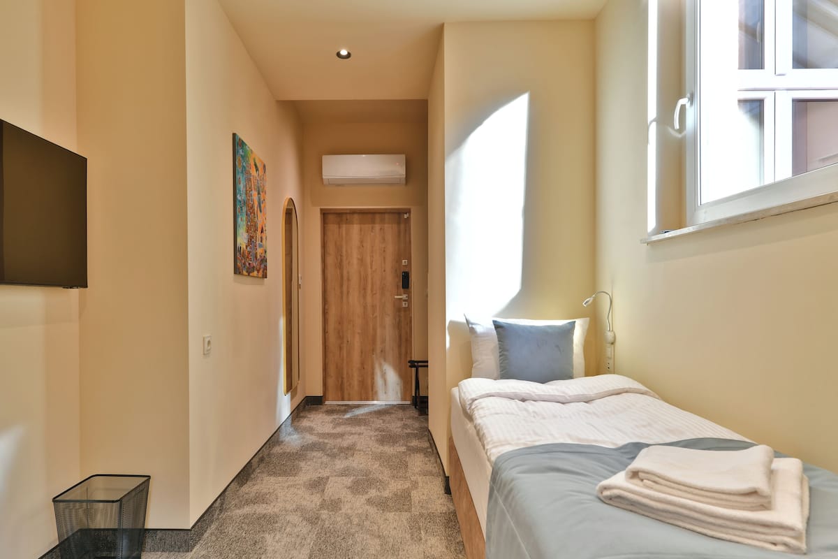 Habitación de hotel con cama, ventana, puerta y televisor montado en la pared.