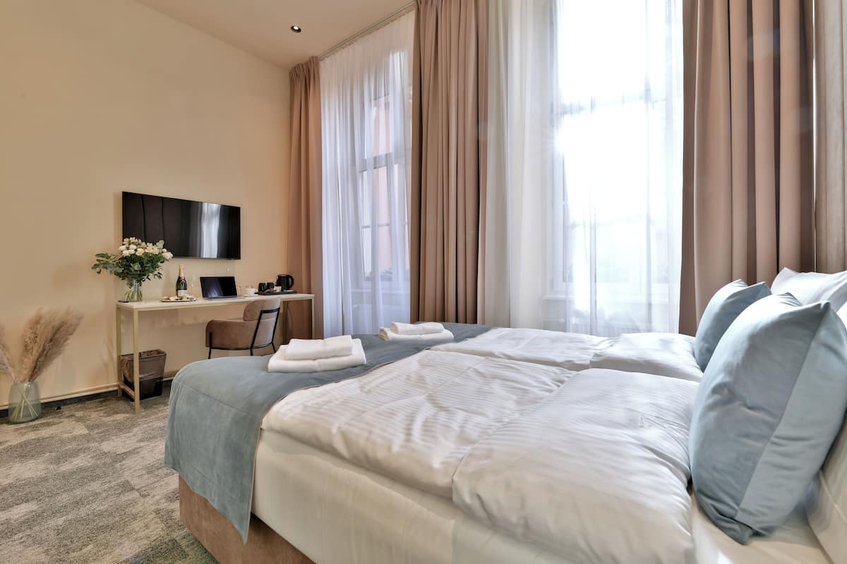 Habitación de hotel con una cama grande, un escritorio con computadora, televisor y ventana con cortinas.