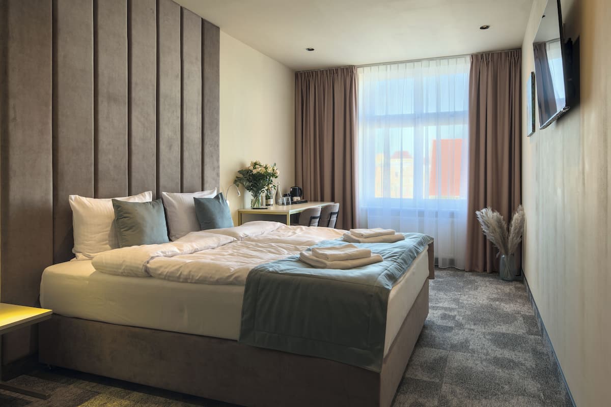 Habitación de hotel con una cama grande, un escritorio, una silla, un televisor y una ventana con cortinas.