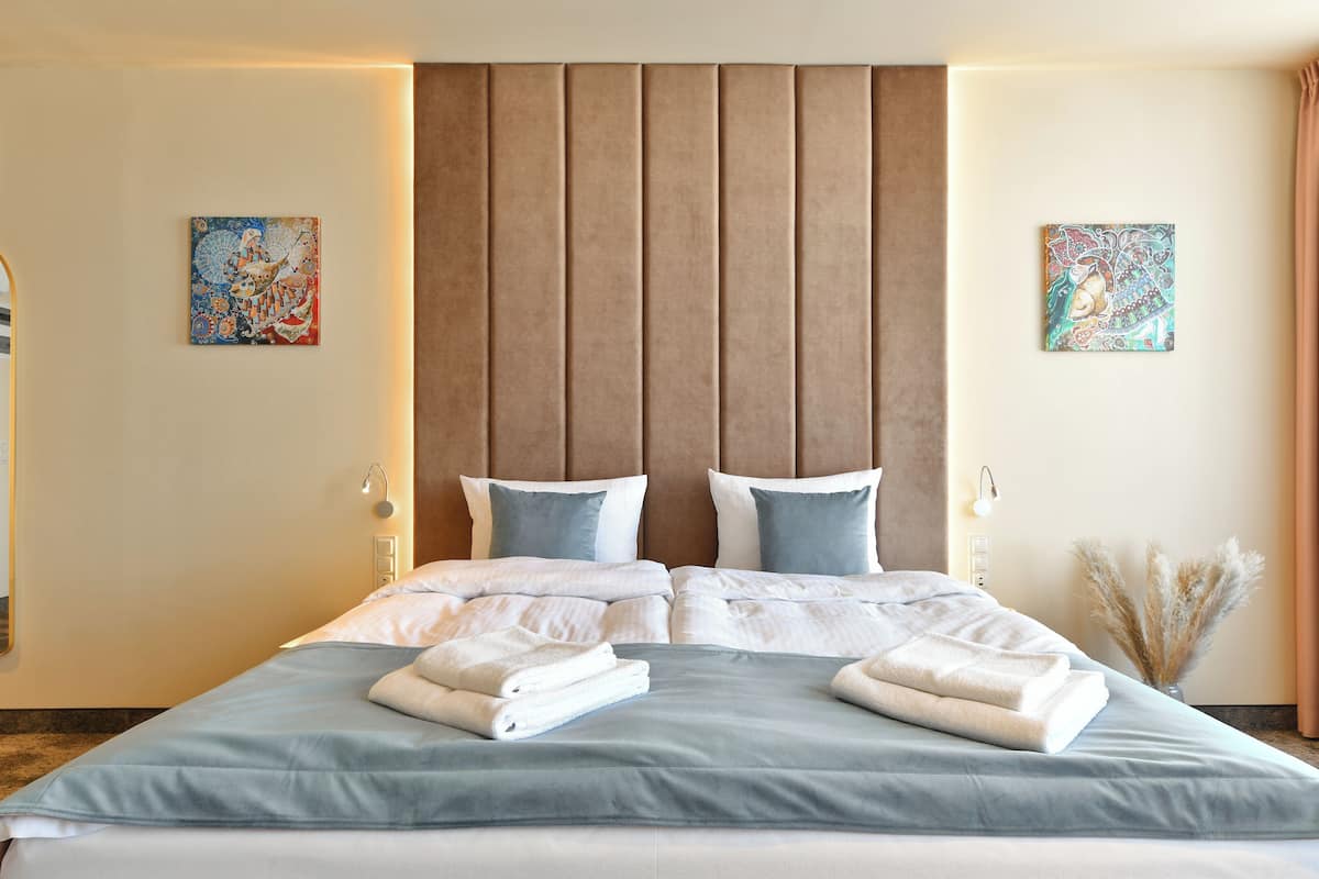 Una habitación de hotel con una cama grande, dos mesitas de noche, un espejo y dos lámparas fijadas a la pared.